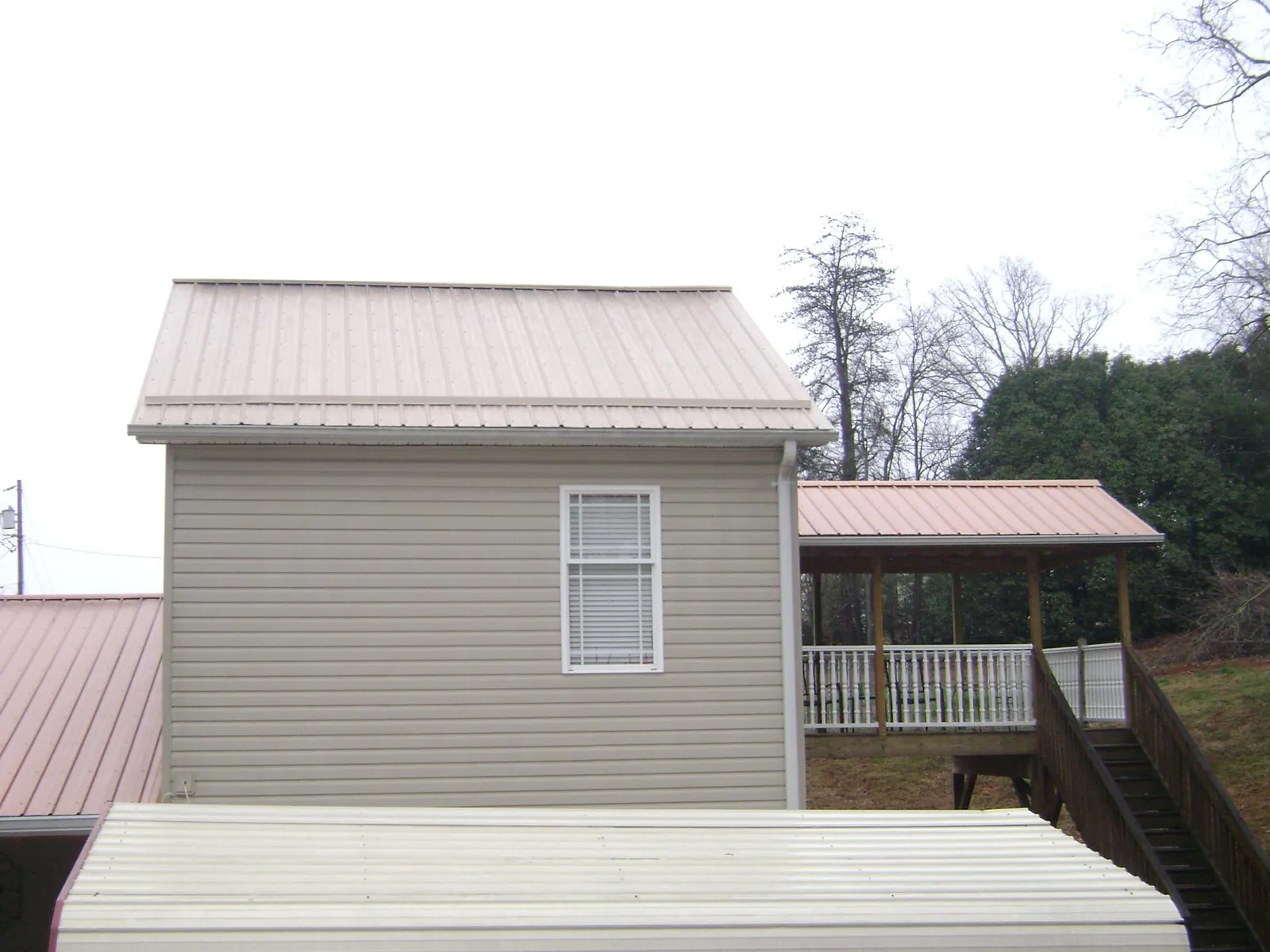 Tan metal roofs on a two story addition and attached porch, from a Roof Replacement job in Brookfield